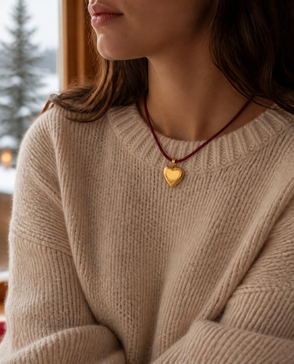Woman wearing the Isla Sol Burgundy Love Necklace, burgundy cord with a gold heart pendant, over a cream knit sweater