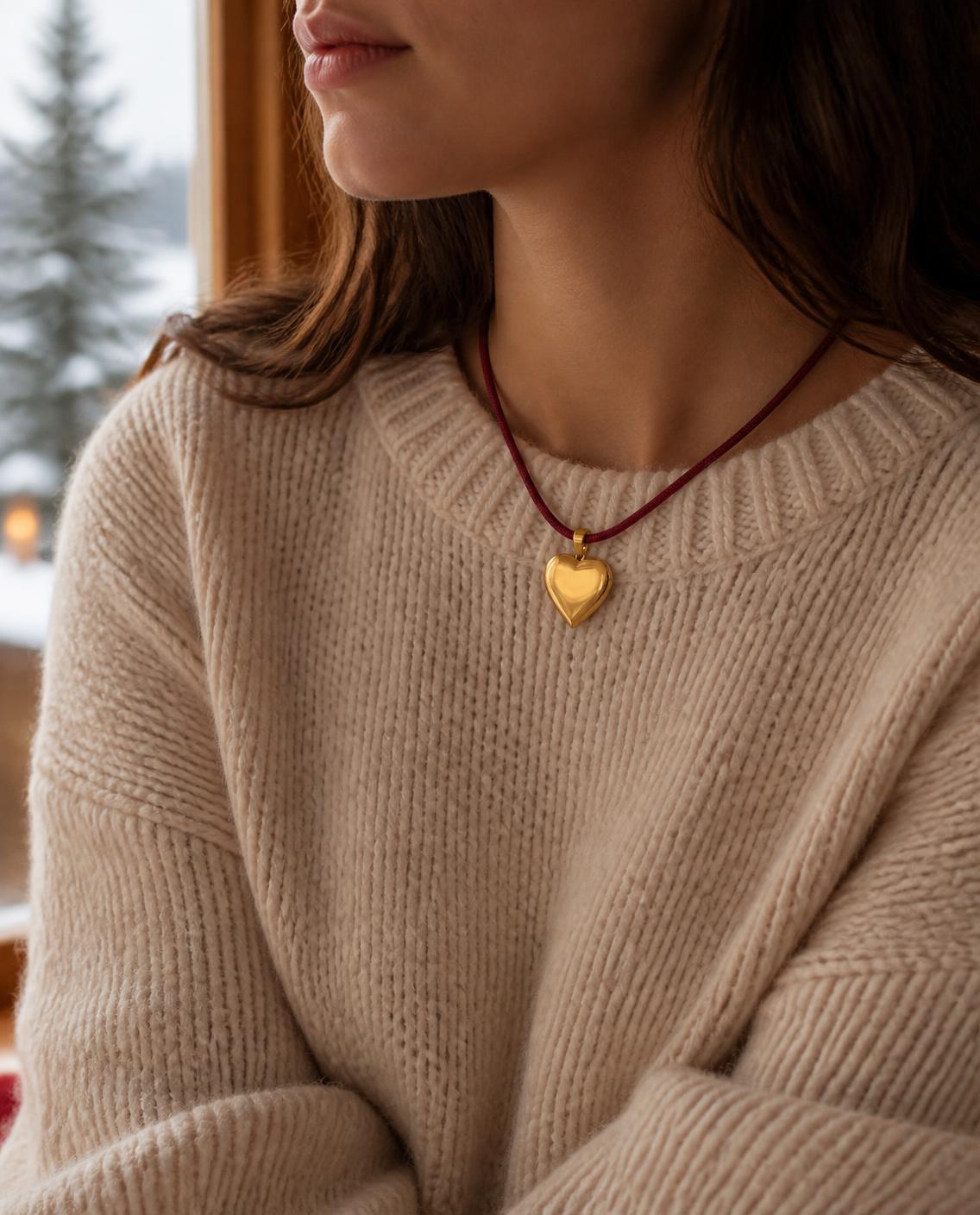 Woman wearing the Isla Sol Burgundy Love Necklace, burgundy cord with a gold heart pendant, over a cream knit sweater