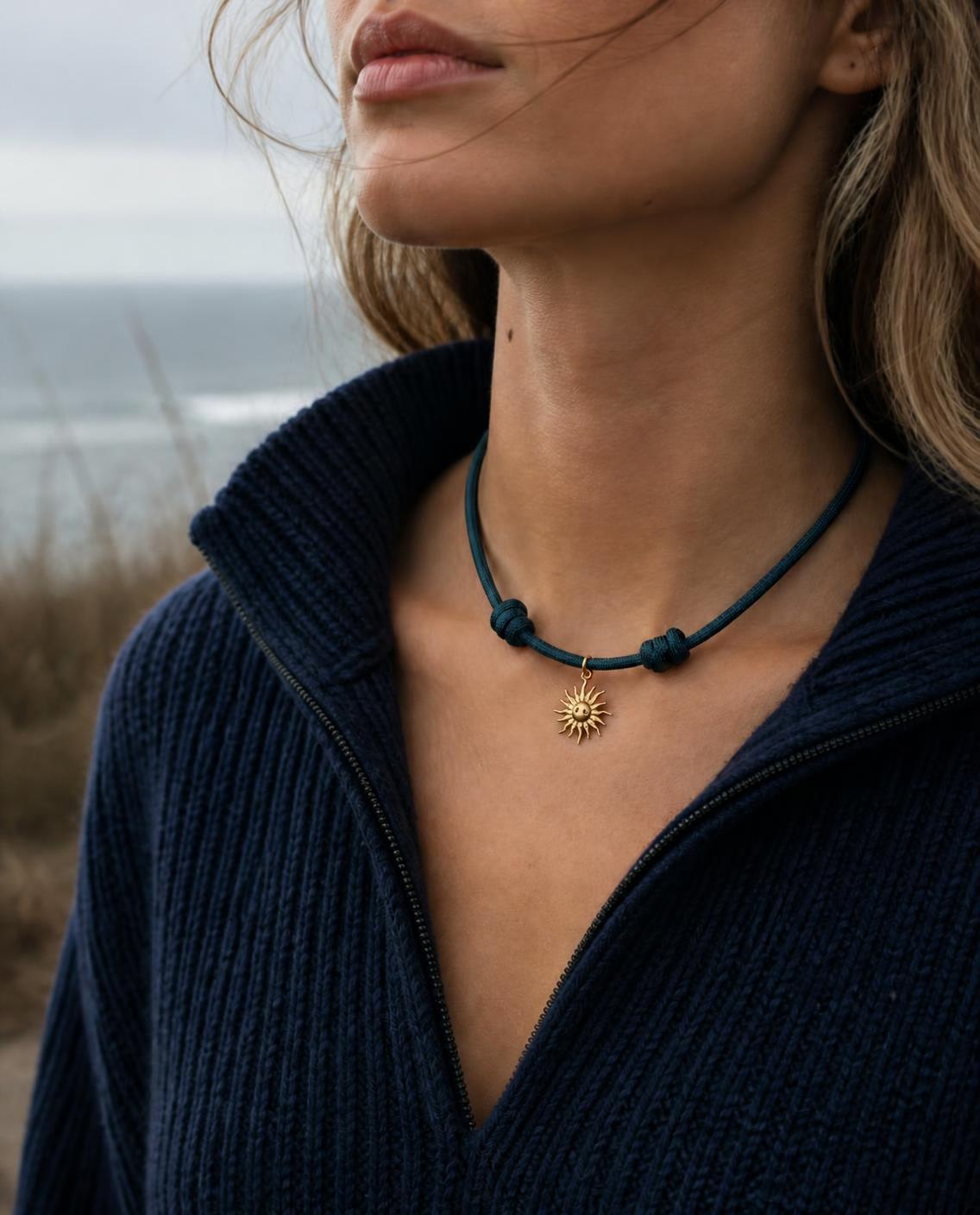 Woman wearing the Isla Sol Midnight Solstice Necklace, deep teal paracord with a gold sun charm, on the California coast