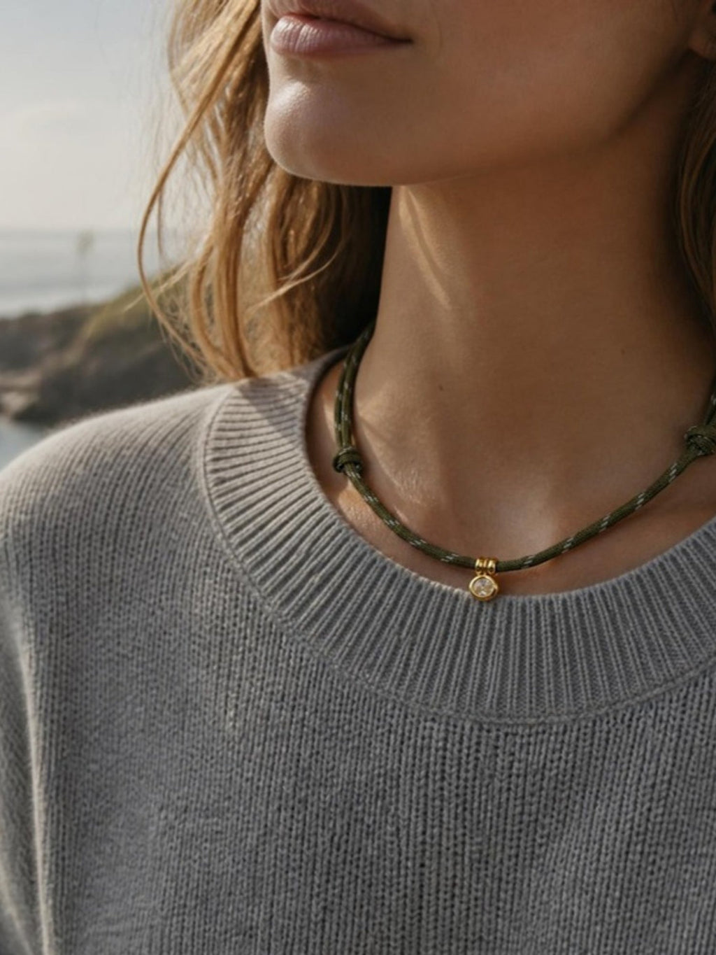 Woman wearing the Isla Sol Summit Necklace in Moss green paracord with a gold bezel charm and a gray sweater