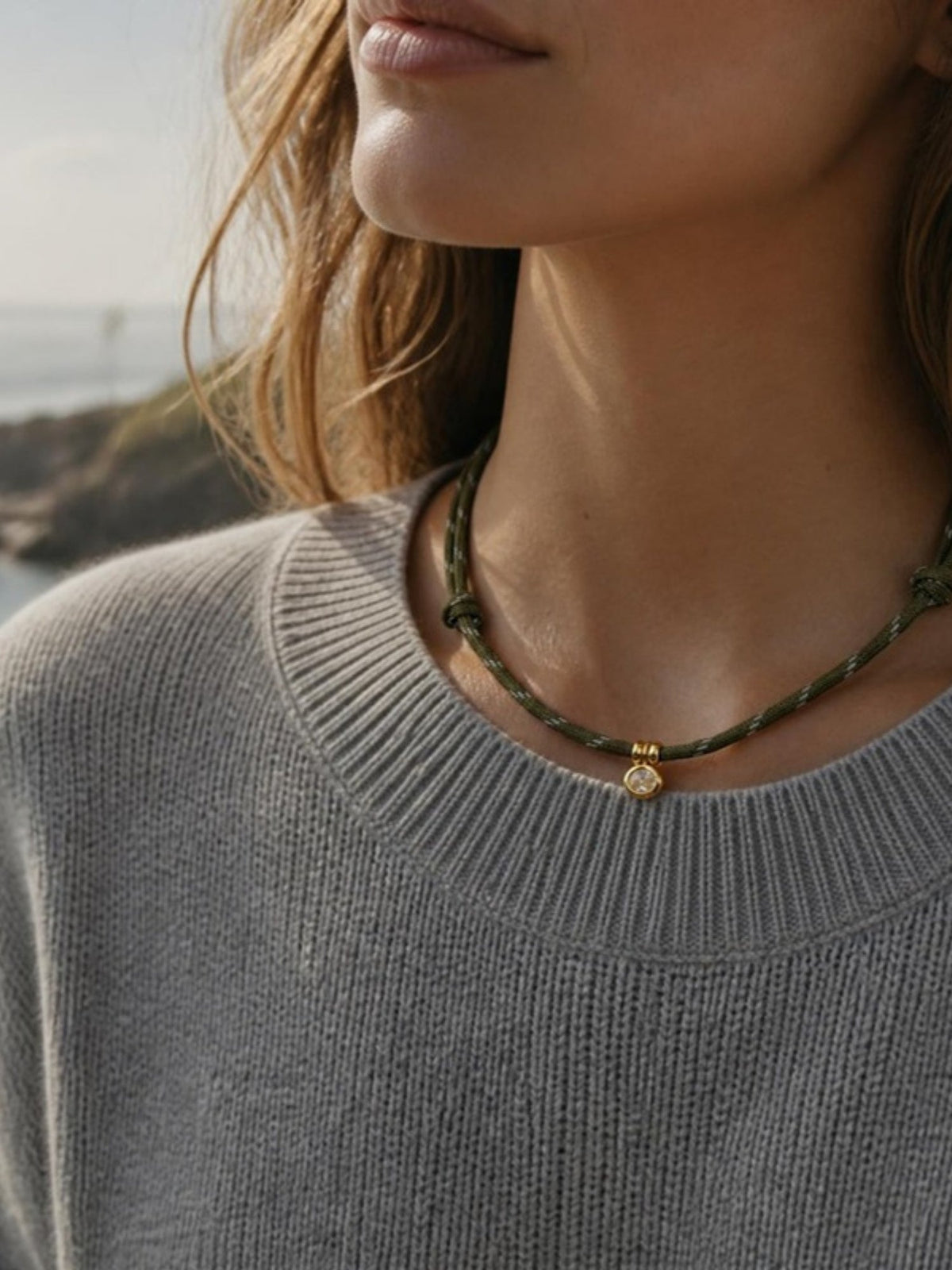 Woman wearing the Isla Sol Summit Necklace in Moss green paracord with a gold bezel charm and a gray sweater